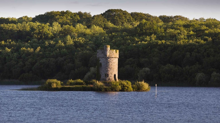 A view across Lough Erne to Crichton Tower standing on Gad Island, with trees in the background and a blue sky above